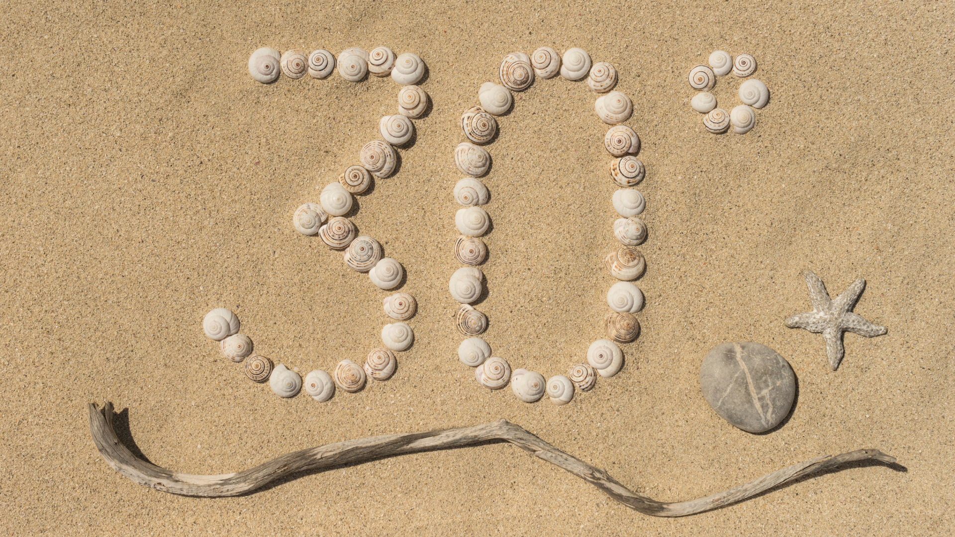 The number 30° is formed with shells on sand, a driftwood stick underneath and a summer value card to the right of a stone and a starfish.