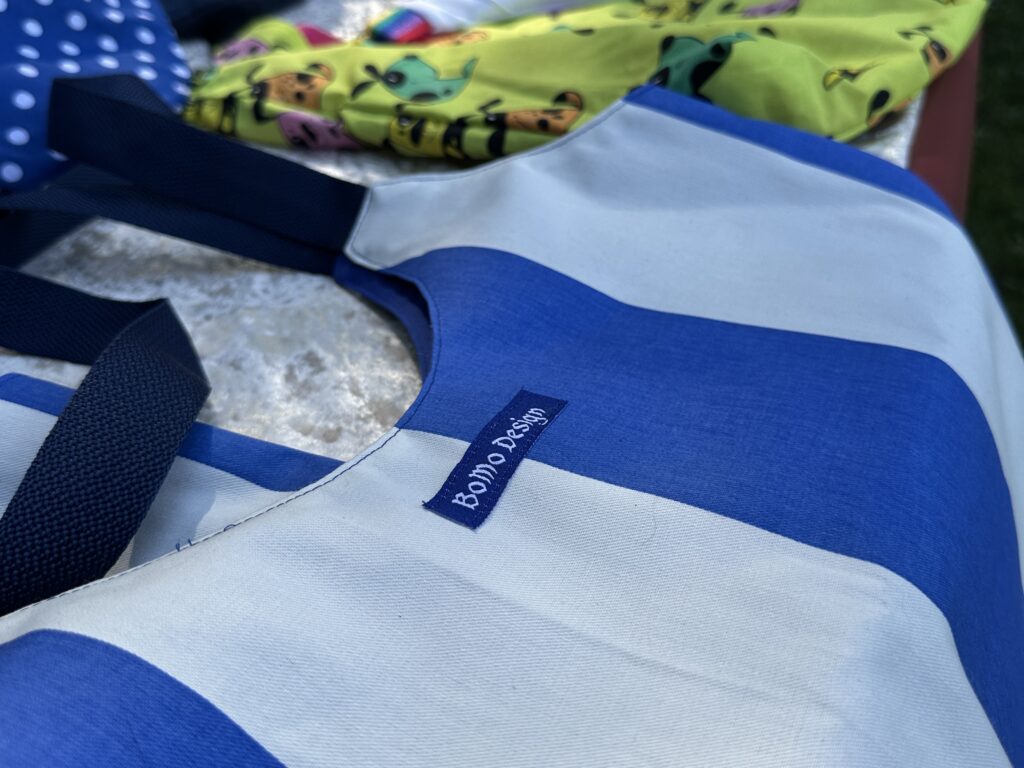 Close-up of a blue and white striped tote bag with a "Bondi Beach" label, next to colorful, patterned fabrics and a summer prepaid card in the background.