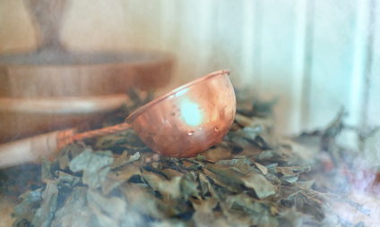 A copper trowel rests on a bundle of dried leaves. Steam or mist swirl around and create a gentle, ethereal atmosphere - perfect for a refreshing cold kick according to Kneipp.